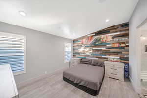 Bedroom featuring light hardwood / wood-style flooring, wooden walls, and vaulted ceiling