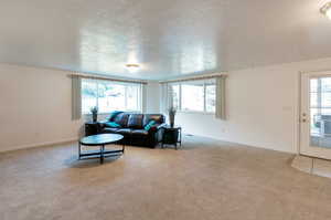 Living room with a textured ceiling, light colored carpet, and a wealth of natural light