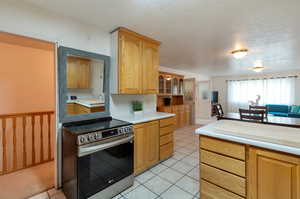 Kitchen featuring light tile patterned flooring, a textured ceiling, light brown cabinets, and stainless steel range with electric cooktop