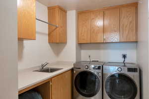 Clothes washing area featuring sink, a textured ceiling, separate washer and dryer, and cabinets