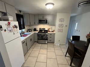 Kitchen with light tile patterned flooring, appliances with stainless steel finishes, sink, and gray cabinets