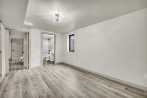 Unfurnished bedroom with connected bathroom, light wood-type flooring, and a textured ceiling