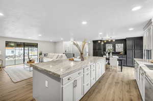 Kitchen with white cabinets, a kitchen island, stainless steel dishwasher, light hardwood / wood-style floors, and light stone counters