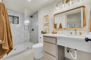 Bathroom with a shower with shower door, vanity, tile patterned flooring, and toilet