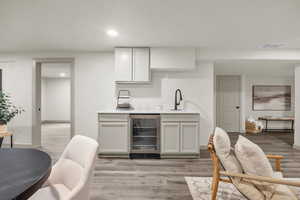 Kitchen featuring wine cooler, sink, light hardwood / wood-style flooring, and white cabinetry