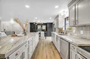 Kitchen featuring light wood-type flooring, dishwasher, light stone countertops, backsplash, and sink