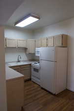 Kitchen with light brown cabinetry, sink, dark hardwood / wood-style flooring, and white appliances