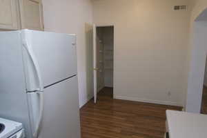 Kitchen with white refrigerator, dark wood-type flooring, and light brown cabinets