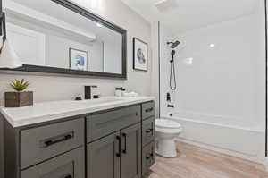 Full bathroom with hardwood / wood-style floors, vanity, tiled shower / bath, and toilet