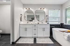 Bathroom with tile patterned floors, dual bowl vanity, and toilet