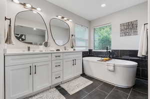 Bathroom featuring a tub, tile walls, dual vanity, and tile patterned flooring