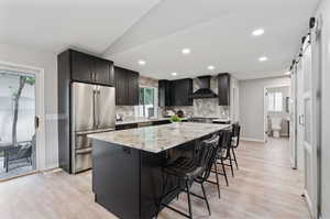 Kitchen with appliances with stainless steel finishes, a barn door, custom exhaust hood, and a healthy amount of sunlight