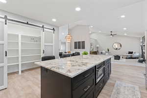 Kitchen featuring a barn door, light wood-type flooring, vaulted ceiling, ceiling fan, and decorative light fixtures