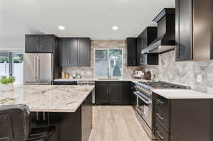 Kitchen with light hardwood / wood-style flooring, high end appliances, plenty of natural light, and wall chimney exhaust hood