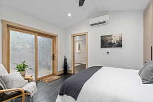 Bedroom featuring a wall mounted air conditioner, dark hardwood / wood-style flooring, ensuite bath, ceiling fan, and vaulted ceiling