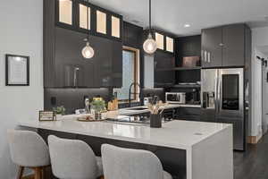 Kitchen with a kitchen breakfast bar, dark hardwood / wood-style flooring, appliances with stainless steel finishes, hanging light fixtures, and sink