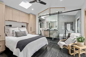 Bedroom with a barn door, a skylight, high vaulted ceiling, ceiling fan, and hardwood / wood-style flooring