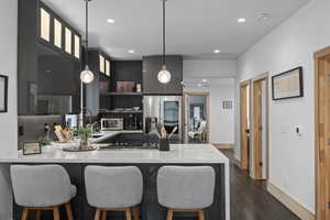 Kitchen with stainless steel appliances, hanging light fixtures, dark wood-type flooring, tasteful backsplash, and sink