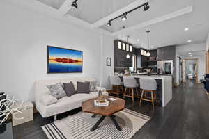 Living room with rail lighting, beamed ceiling, and dark wood-type flooring