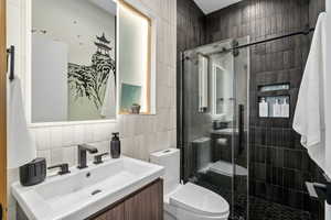 Bathroom with a shower with shower door, tile walls, vanity, and toilet