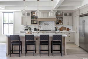 Kitchen with a center island with sink, high end refrigerator, a breakfast bar, backsplash, and light hardwood / wood-style flooring