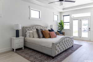 Bedroom with ceiling fan, light hardwood / wood-style flooring, a tray ceiling, and access to exterior