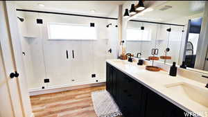 Bathroom featuring dual bowl vanity, hardwood / wood-style flooring, a shower with shower door, and a healthy amount of sunlight