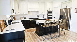 Kitchen with white cabinets, a kitchen breakfast bar, light wood-type flooring, stainless steel appliances, and a kitchen island