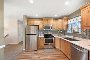 Kitchen featuring stainless steel appliances, light brown cabinetry, light colored carpet, decorative backsplash, and sink