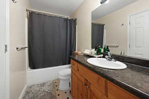 Full bathroom featuring a textured ceiling, toilet, shower / tub combo with curtain, tile patterned floors, and vanity