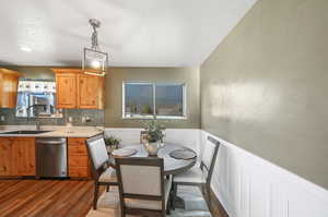 Kitchen featuring stainless steel dishwasher, hanging light fixtures, backsplash, sink, and dark wood-type flooring