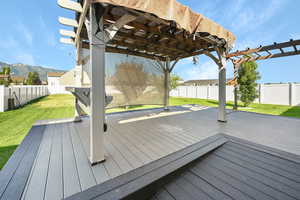 Wooden deck with a pergola, a lawn, and a mountain view