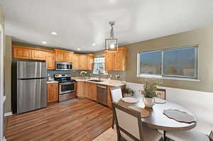 Kitchen with stainless steel appliances, sink, tasteful backsplash, light hardwood / wood-style flooring, and decorative light fixtures