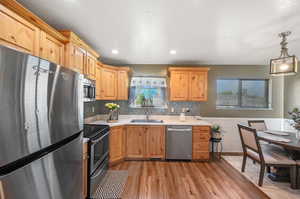 Kitchen featuring tasteful backsplash, appliances with stainless steel finishes, light hardwood / wood-style flooring, sink, and decorative light fixtures