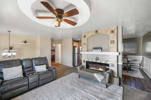 Living room with a textured ceiling, carpet, ceiling fan, and a raised ceiling