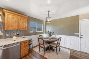 Interior space with light brown cabinets, dishwasher, decorative light fixtures, tasteful backsplash, and dark hardwood / wood-style flooring