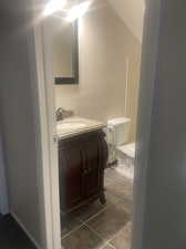 Bathroom featuring tile patterned floors, vanity, vaulted ceiling, and toilet