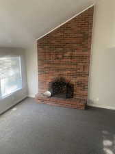 Unfurnished living room featuring vaulted ceiling, a fireplace, and new carpet