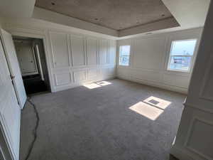 Master bedroom with light colored carpet, multiple windows, and a tray ceiling