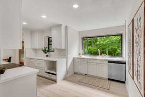 Kitchen featuring light wood-type flooring, white cabinets, dishwasher, and sink