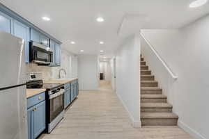 Kitchen featuring light wood-type flooring, blue cabinets, stainless steel appliances, backsplash, and sink