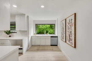 Kitchen with light wood-type flooring, a healthy amount of sunlight, stainless steel dishwasher, and white cabinetry