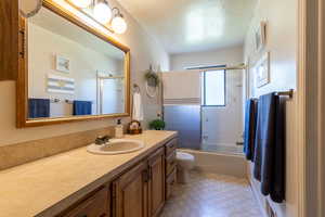 Full bathroom featuring shower / bath combination with glass door, toilet, vanity, and tile patterned flooring