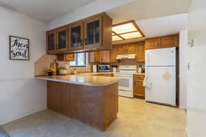 Kitchen with white appliances, sink, kitchen peninsula, and light tile patterned floors