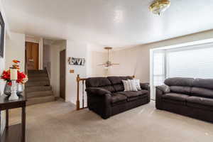 Living room featuring ceiling fan, a textured ceiling, and light colored carpet