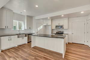 Kitchen with stainless steel appliances, white cabinets, light wood-type flooring, and sink