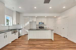 Kitchen with appliances with stainless steel finishes, white cabinetry, a center island, and light hardwood / wood-style flooring