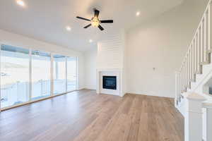 Unfurnished living room featuring a fireplace, high vaulted ceiling, ceiling fan, and light wood-type flooring