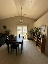 Tiled dining space with lofted ceiling, a textured ceiling, and a notable chandelier