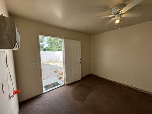 Carpeted spare room/office space in 1/2 of 3rd car garage space with ceiling fan and a wall mounted AC and heater, door to side yard.